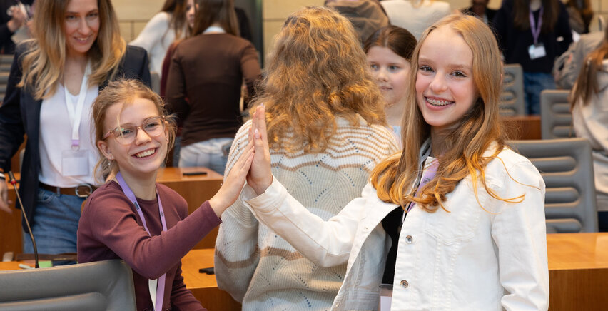 Zwei Schüler:innen im Landtag NRW, die abklatschen und in die Kamera lächeln